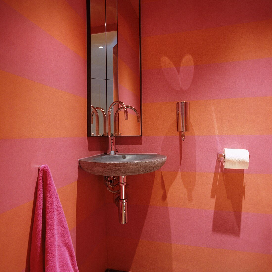 Eckwaschbecken aus Stein und Spiegelschrank in rosa-orange-farben gestreifter Gäste-Toilette