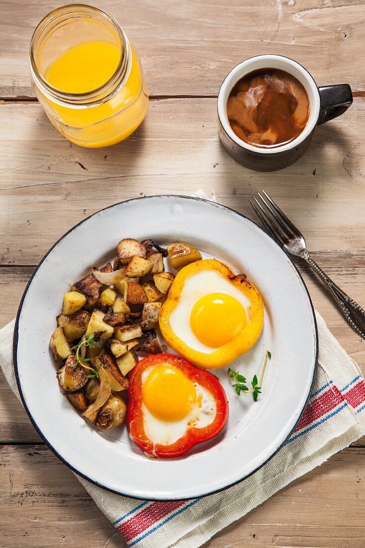 Eier in roter und gelber Paprika mit Bratkartoffeln gebacken, ein Kaffee und Orangensaft