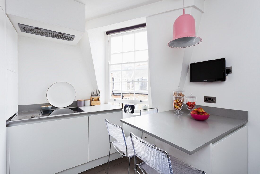 White, modern kitchen with grey console table and pink, bell-shaped pendant lamp