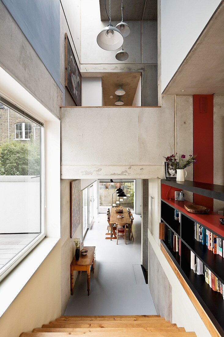 Open-plan, multi-level interior with exposed concrete; pale wooden stairs in foreground leading to dining area