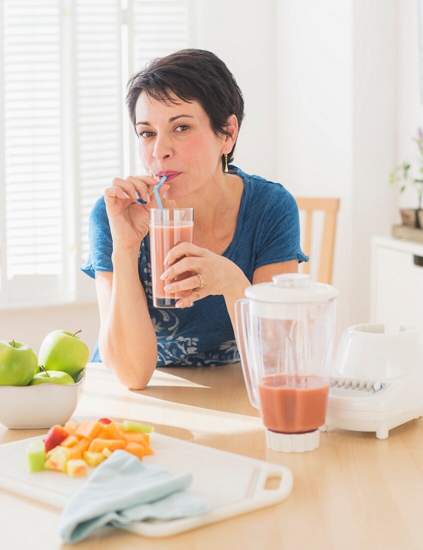 A woman drinking a smoothie in the kitchen
