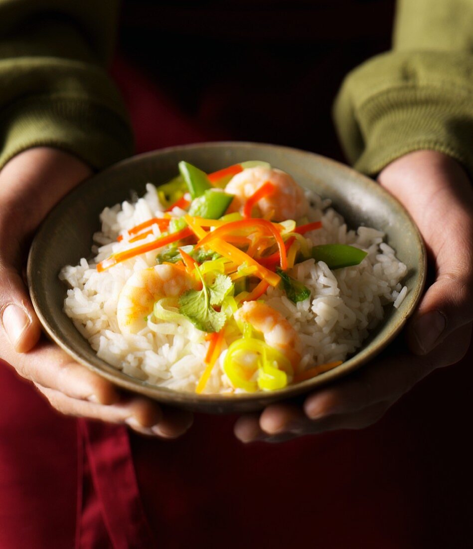 Hands holding a dish of vegetable rice with prawns