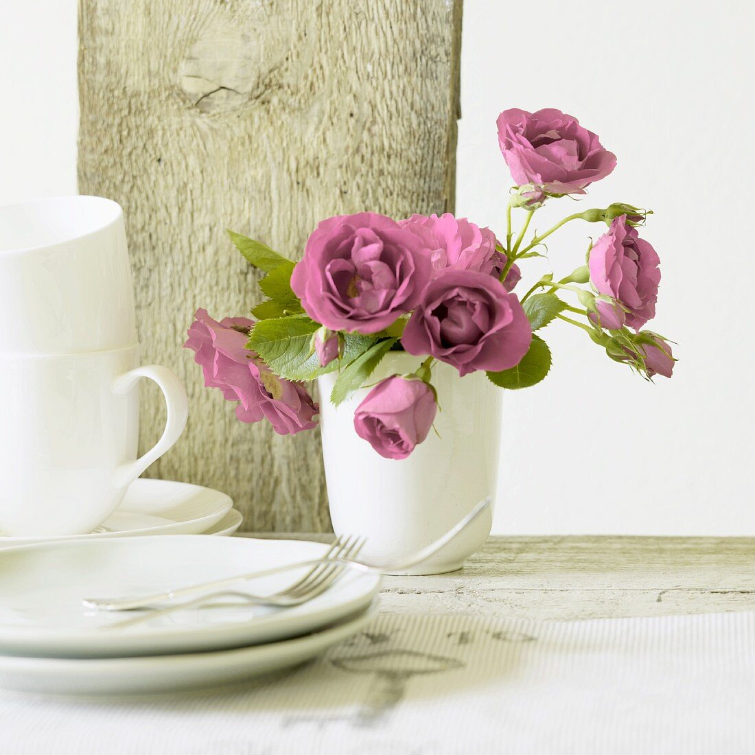 Pink roses in ceramic vase, teacups and side plates