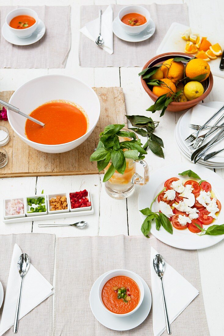 Gedeckter Tisch mit Gazpacho, Tomaten und Mozzarella, Orangen und Zitronen