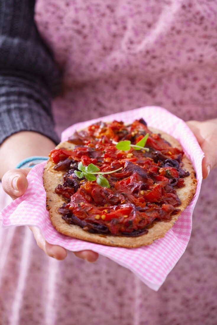 A woman holding a wholemeal pizza topped with peppers and onions