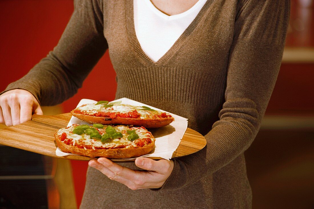 A woman serving small pizzas on a wooden bread peel