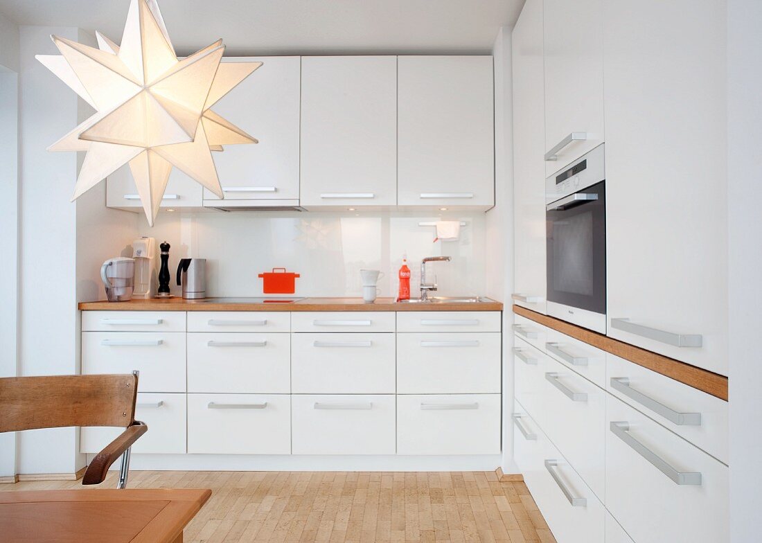 Küche mit weissen Möbeln, Holzarbeitsplatte, Einbauherd, Holzboden und Sternlampe