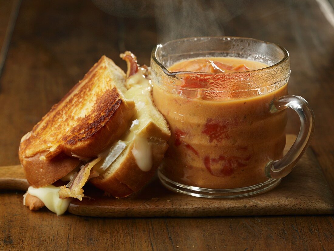 Halber Sandwichtoast mit Käse und Bacon und einer Tasse würfeliger Tomatensuppe