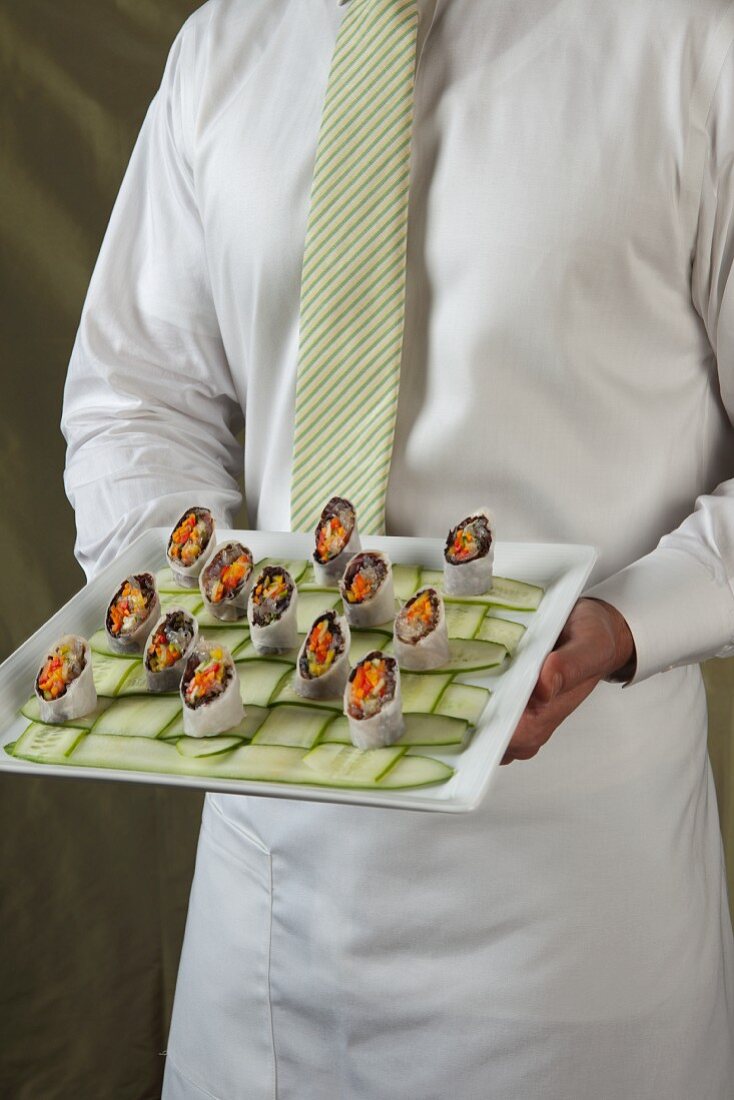 Kellner hält ein Tablett mit Asia-Wraps auf Gurkenstreifen