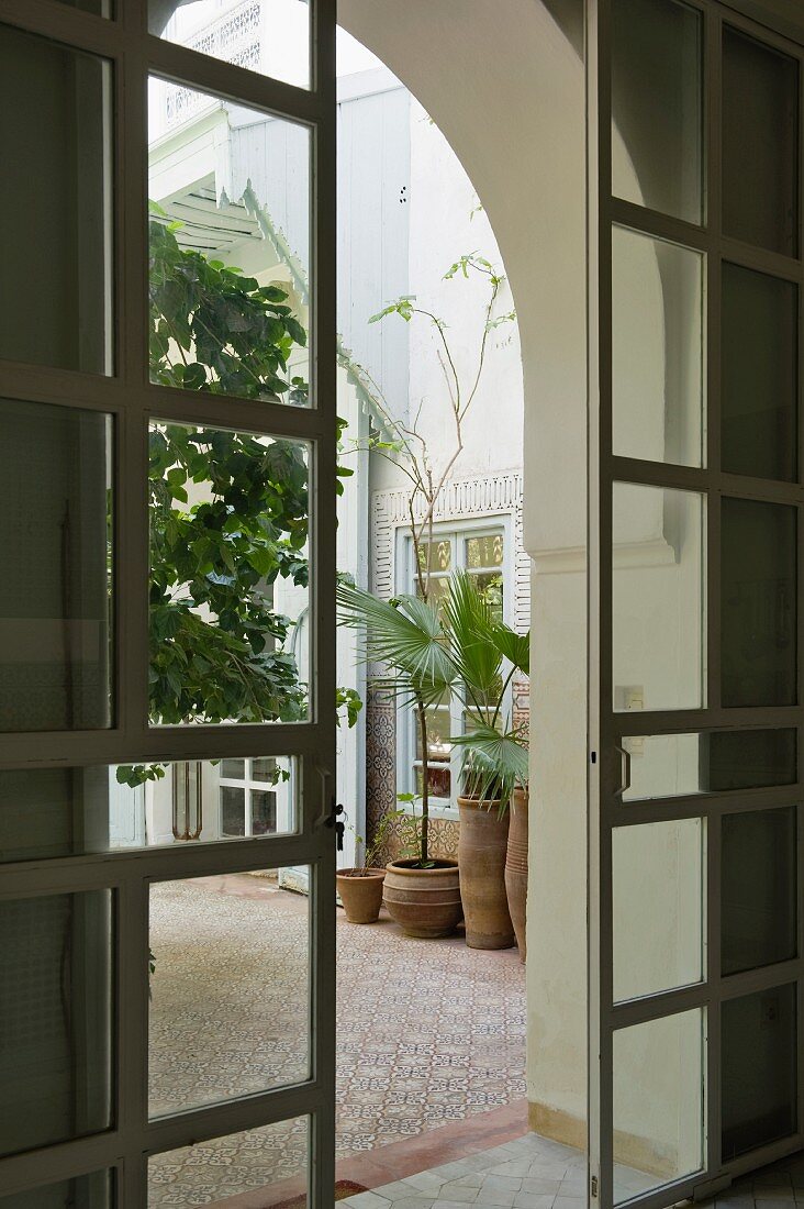 View though open sliding doors into Moroccan courtyard with potted plants on mosaic tiles