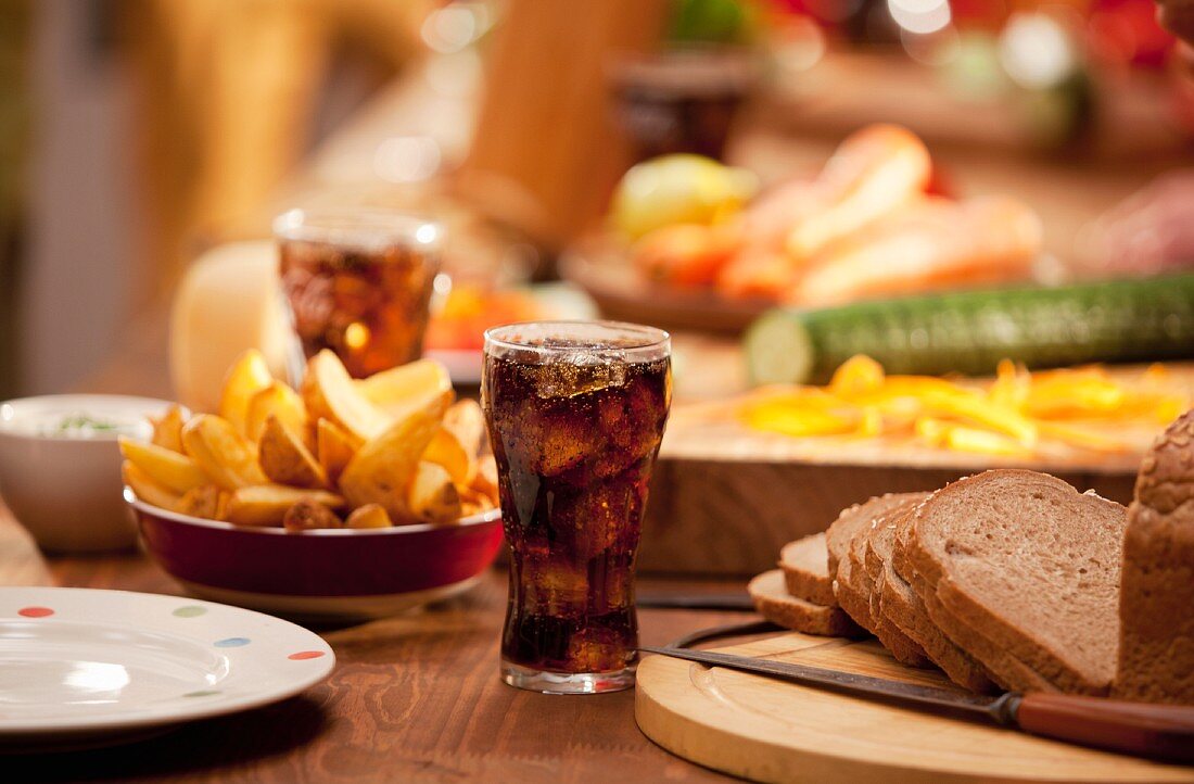 A table set with bread, potato wedges, raw vegetables and cola