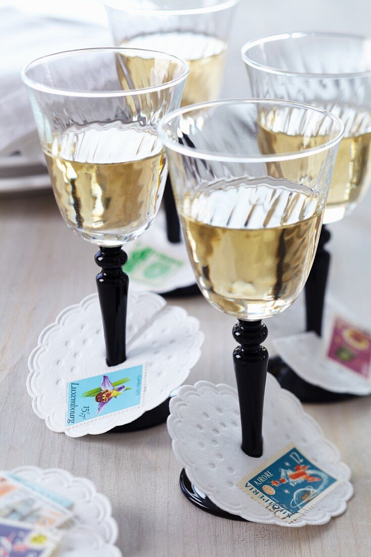 Paper collars decorated with postage stamps as wine glass drip catchers