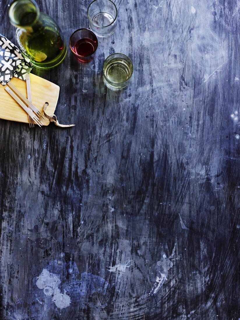 Sicht auf blauen Holztisch mit Olivenöl, Gläser mit Wein und Holzbrett mit Gabeln