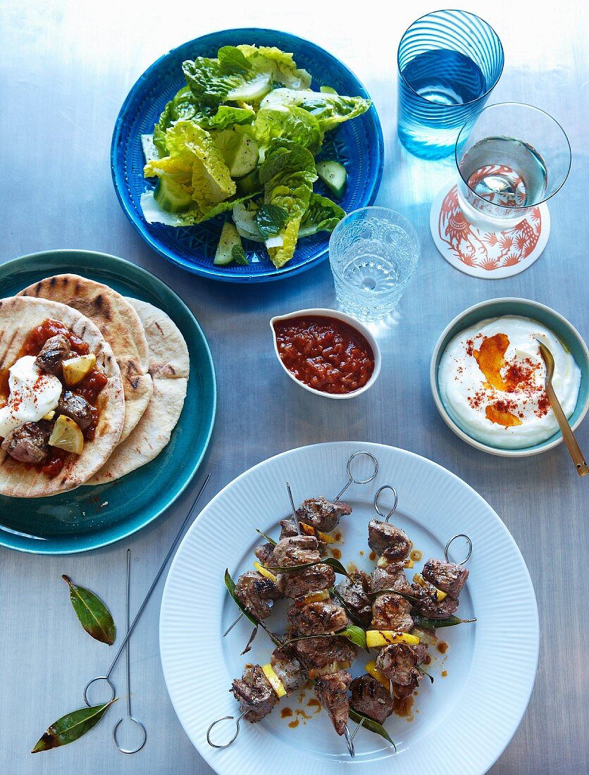 Souflaki skewers with pork, lemons and bay leaves served with tzatziki, tomato sauce, pita bread and salad