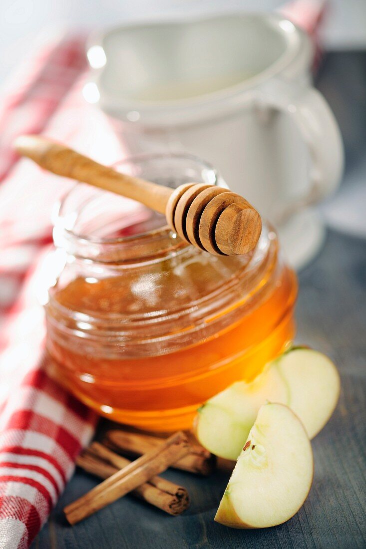 Honig im Glas; daneben Zimtstangen und Apfelschnitze