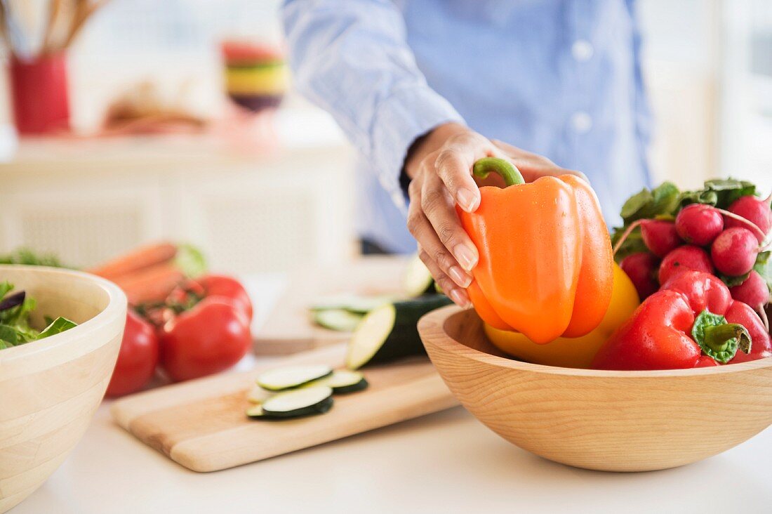 A hand taking a pepper from a wooden bowl of vegetables