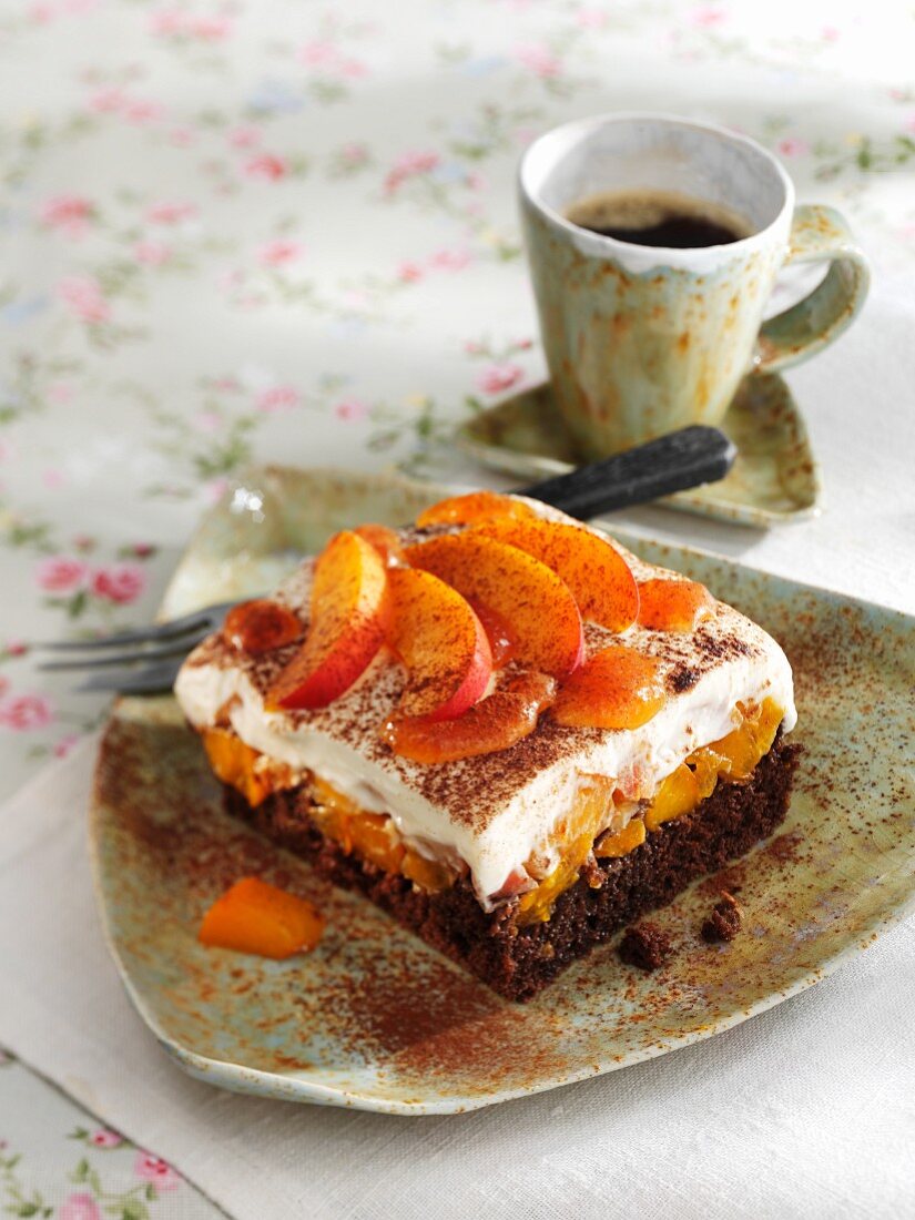 A square of chocolate cake topped with apricots and thickened cream