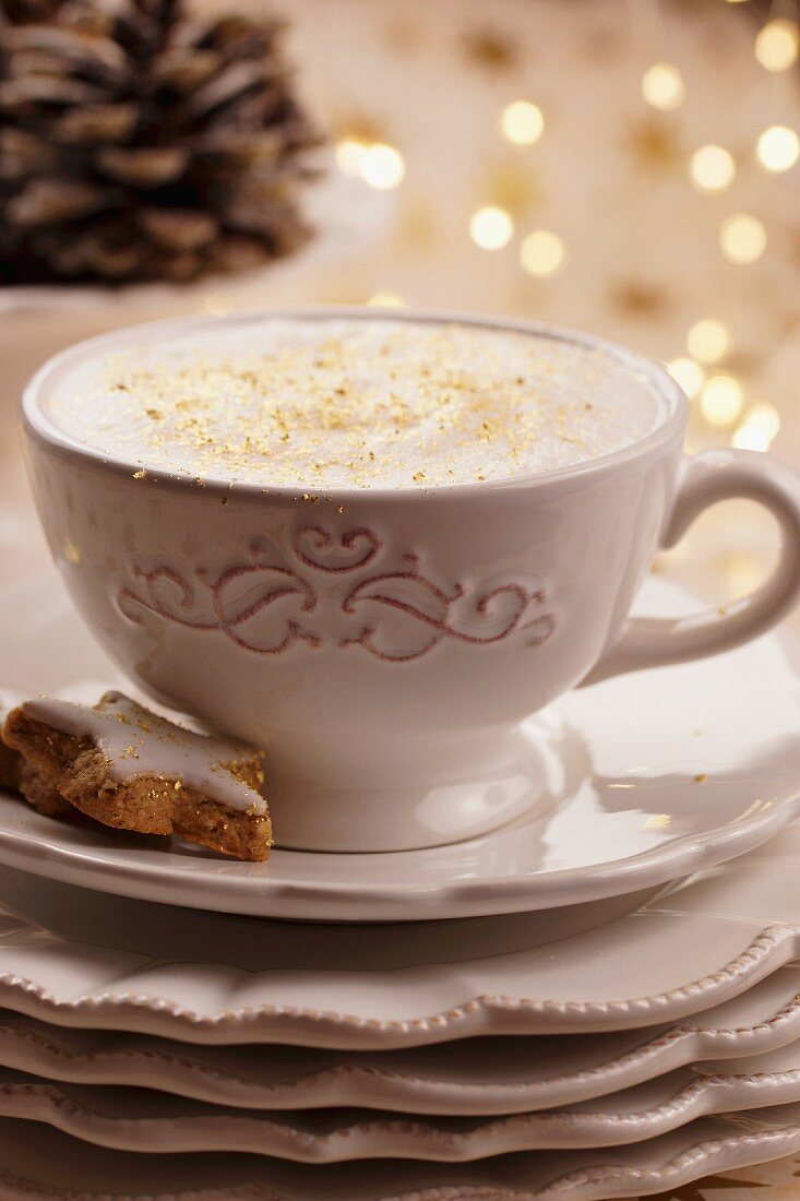 Cappuccino with gold sprinkles and a star-shaped cinnamon biscuit