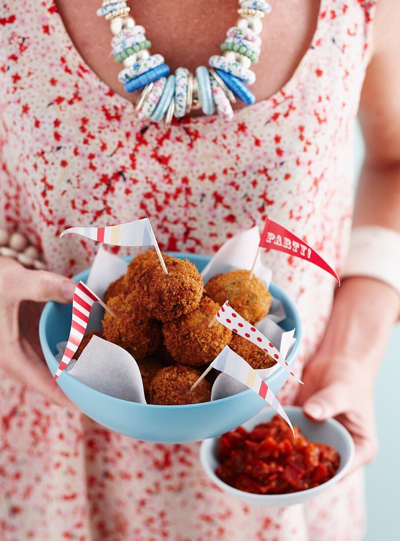 A woman holding a bowl of meatballs and spicy salsa for a party
