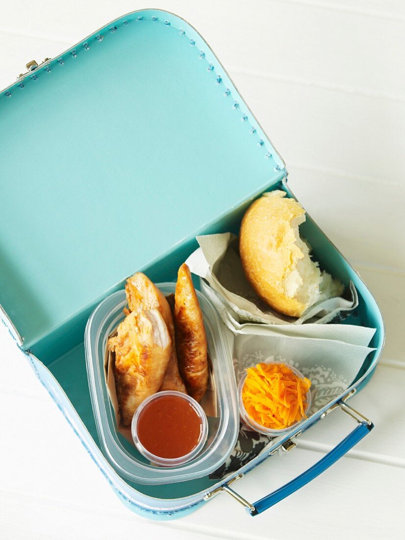 Teriyaki chicken with a dip, a bread roll and a carrot salad in a lunch box