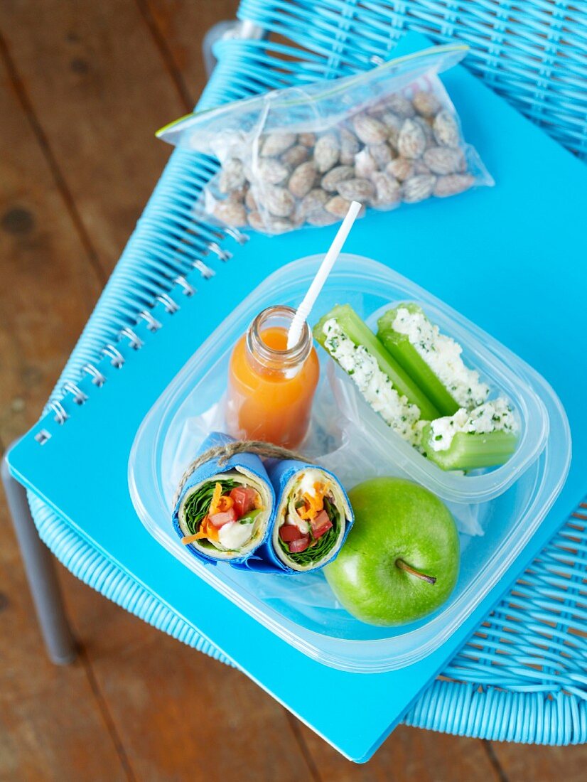 Wraps, cucumber, an apple and juice in a lunch box