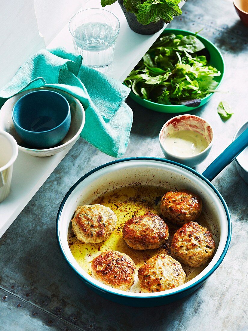 Lemon chicken meatballs in a saucepan with a mixed leaf salad and a mint dressing in the background