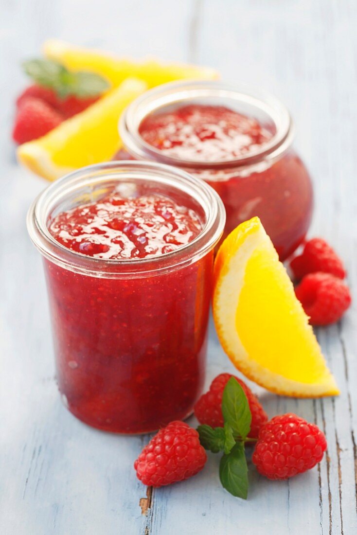 Two jars of orange and raspberry jam on a wooden surface