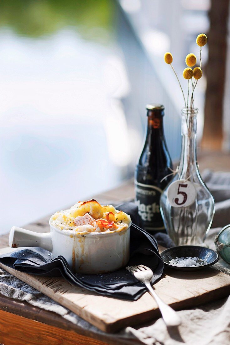 A mini fish bake in a ramekin on a wooden table laid with maritime decorations