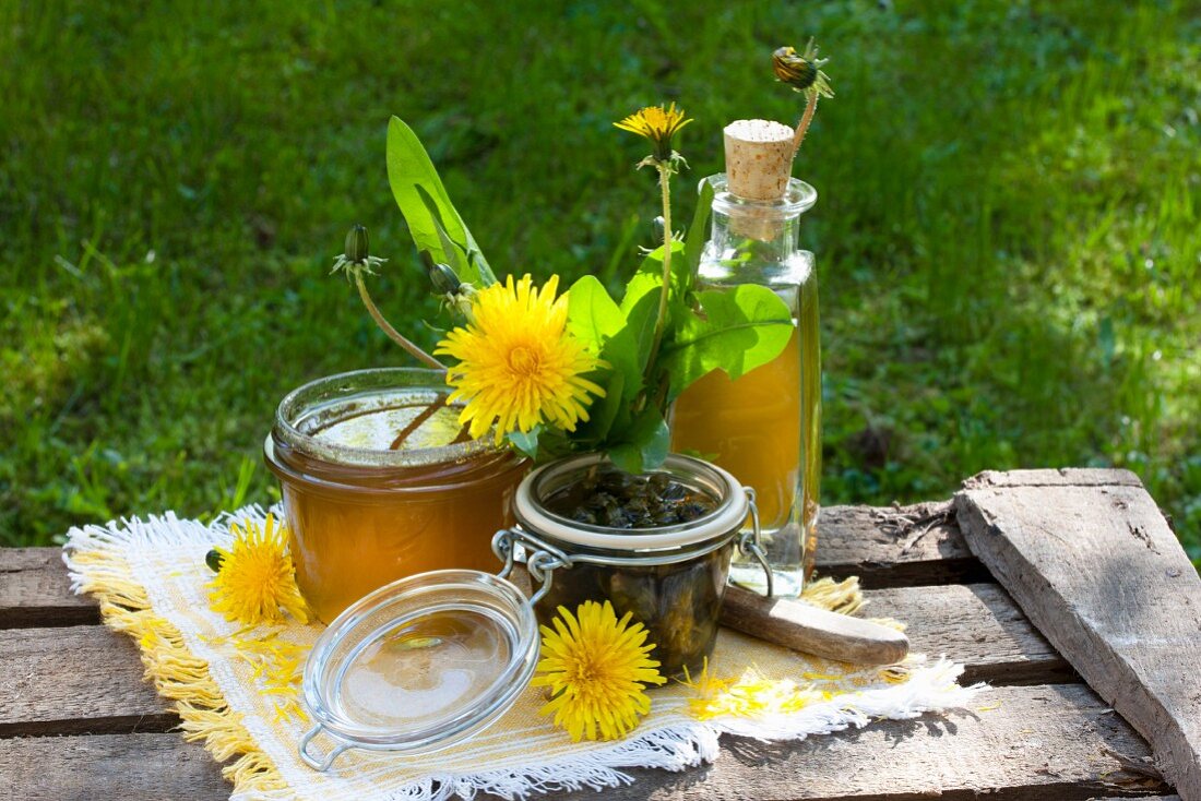 Various dandelion products; jelly, liqueur and pickled buds on wooden boards