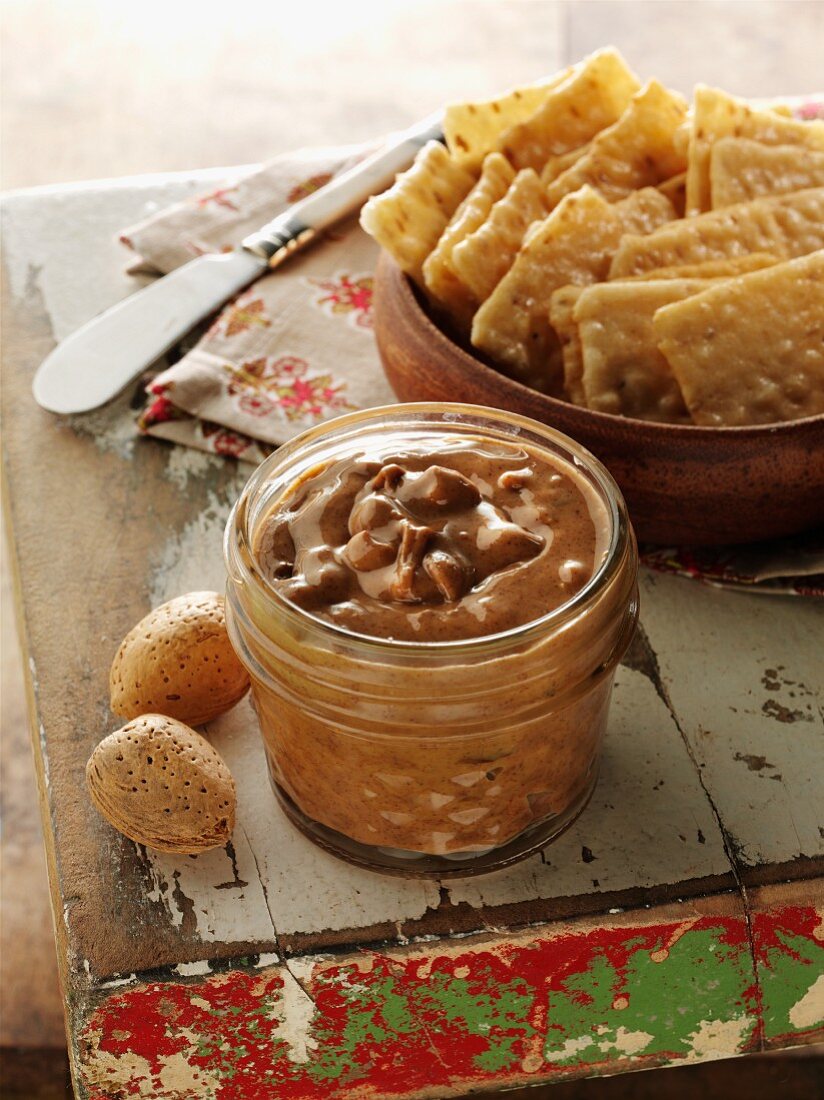 Jar of organic chunky Almond nut butter on old wood pedestal with crackers