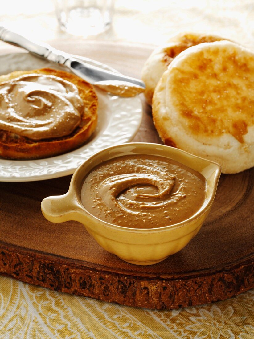 Cup of creamy cashew nut butter on a wood slab with english muffins.