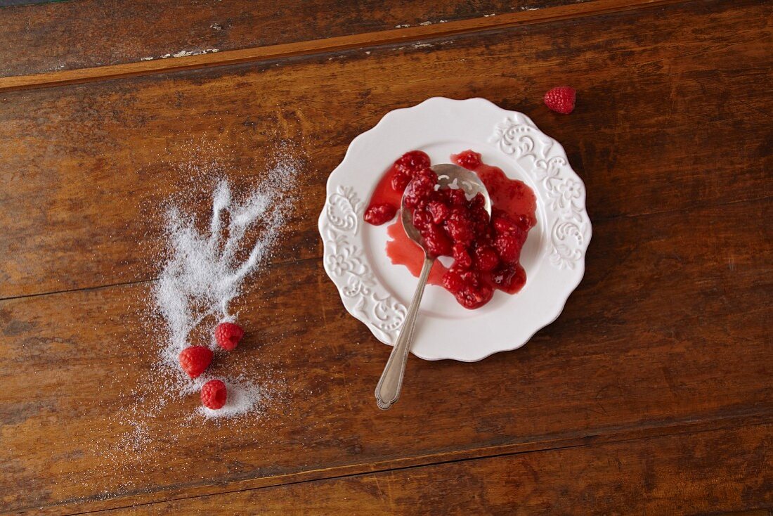 A Ladle with Raspberry Sauce on a White Plate; Fresh Raspberries and Sugar