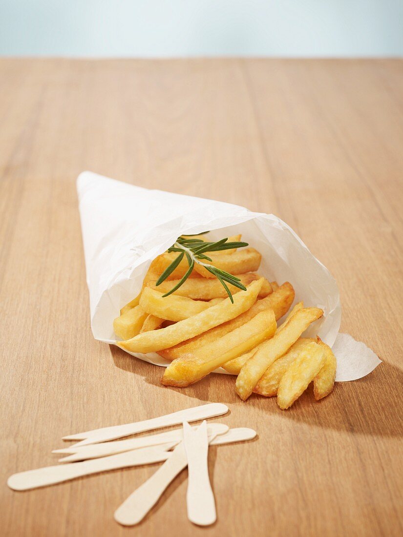 Chips with a sprig of rosemary in a cone of white baking parchment, and wooden chip forks