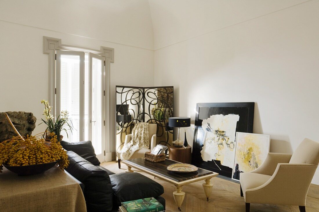 Black sofa and pale armchairs around coffee table in minimalist interior with postmodern ambiance