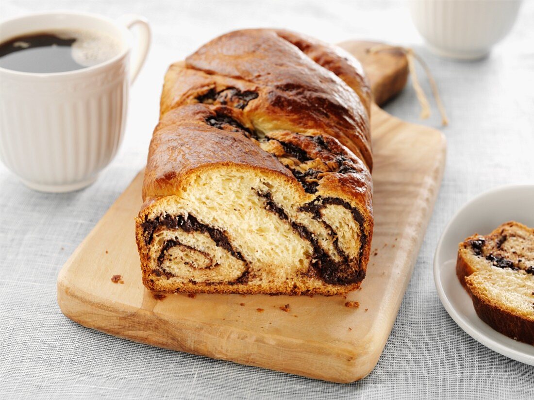 Chocolate Babka loaf on cutting board with slice and cup coffee.