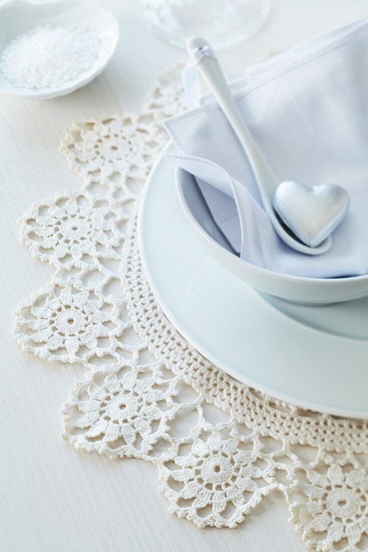 Romantic place setting with silver heart on china spoon and crocheted doily as place mat