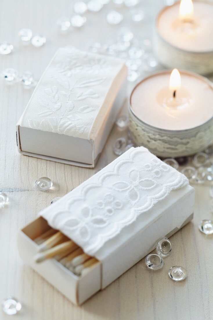 Matchboxes covered in white paper and decorated with lace trim and decorated tealights