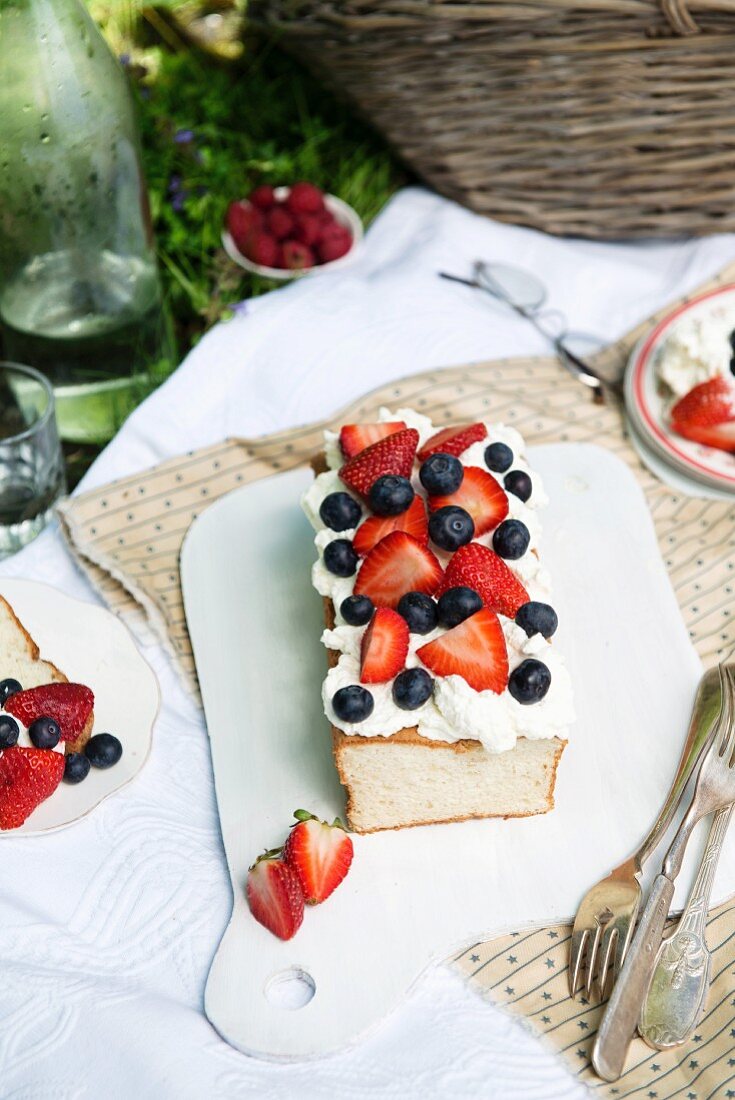 Angel food cake baked in a loaf tin and topped with fresh berries, at a picnic