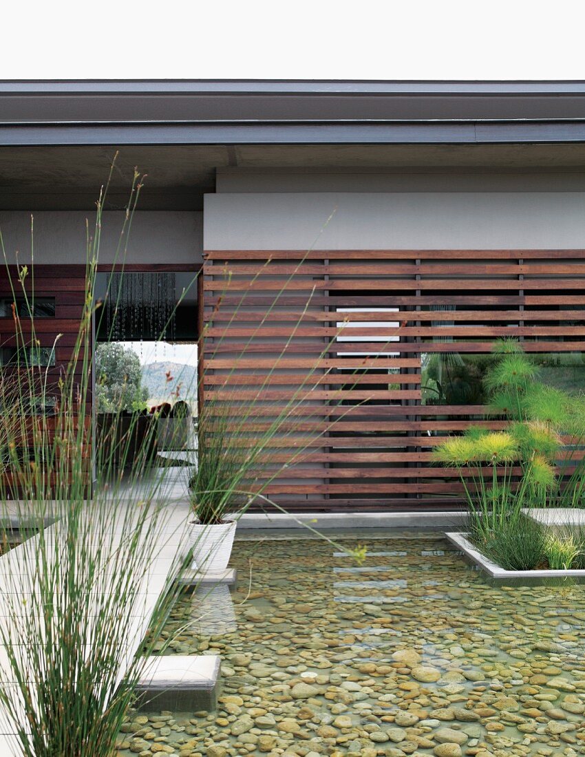 Steg neben Wasserbecken im Garten vor zeitgenössischem Wohnhaus mit Holzlamellen Verkleidung an Fassade