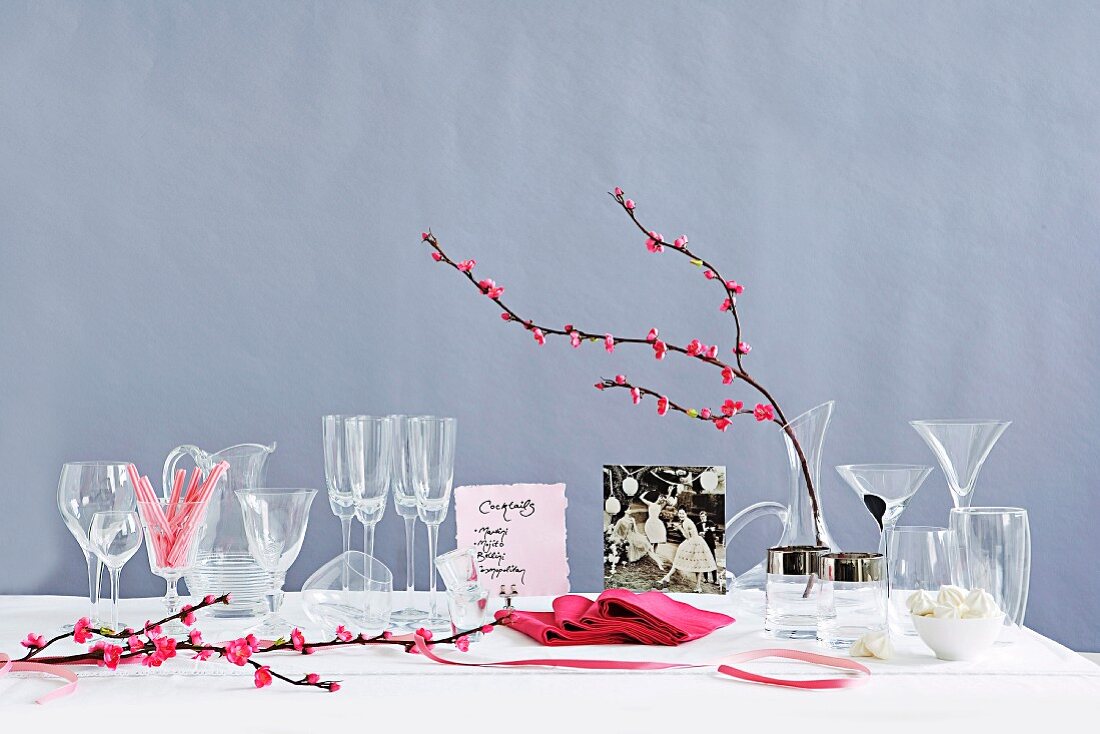 A table laid with assorted glasses, pink napkins and flowering twigs