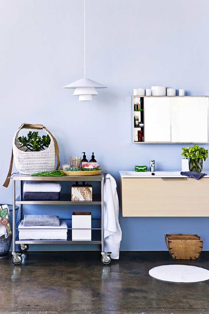 Modern bathroom with mirrored cabinet, sink and trolley of towels and toiletries