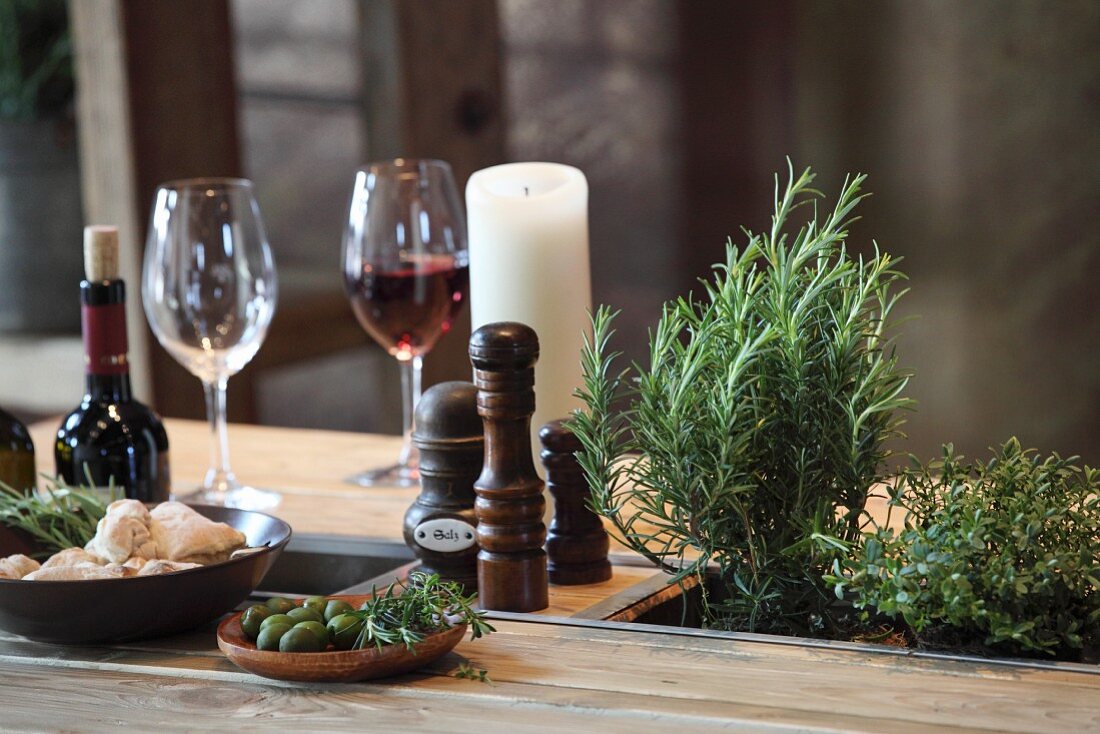 Rustikaler Esstisch aus Palette mit Kräutertöpfen, Kerze und Weingläsern