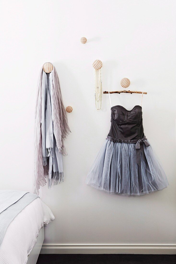 Scarves and short cocktail dress hanging from round wooden knobs on wall next to bed in bedroom