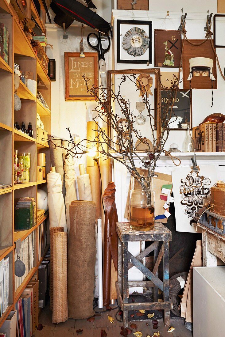 Collection of bolts of fabric, pictures on wall and branches in vase next to next to shelving