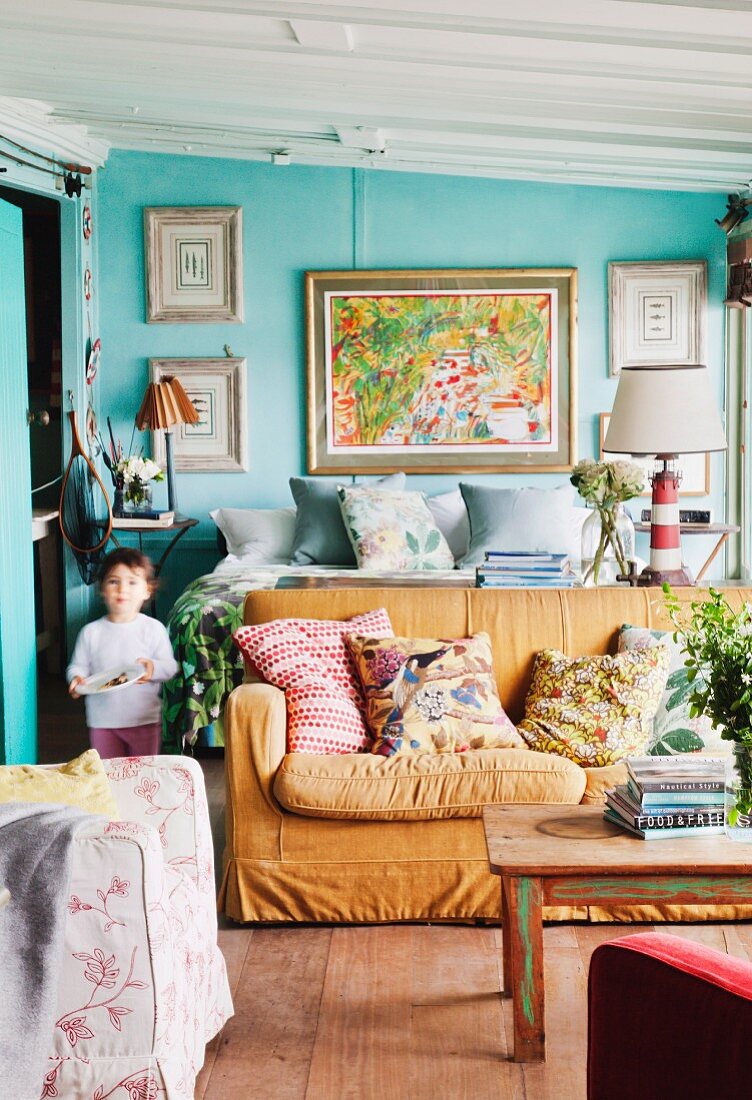 Sofa and double bed in interior with walls painted turquoise and gallery of pictures in background