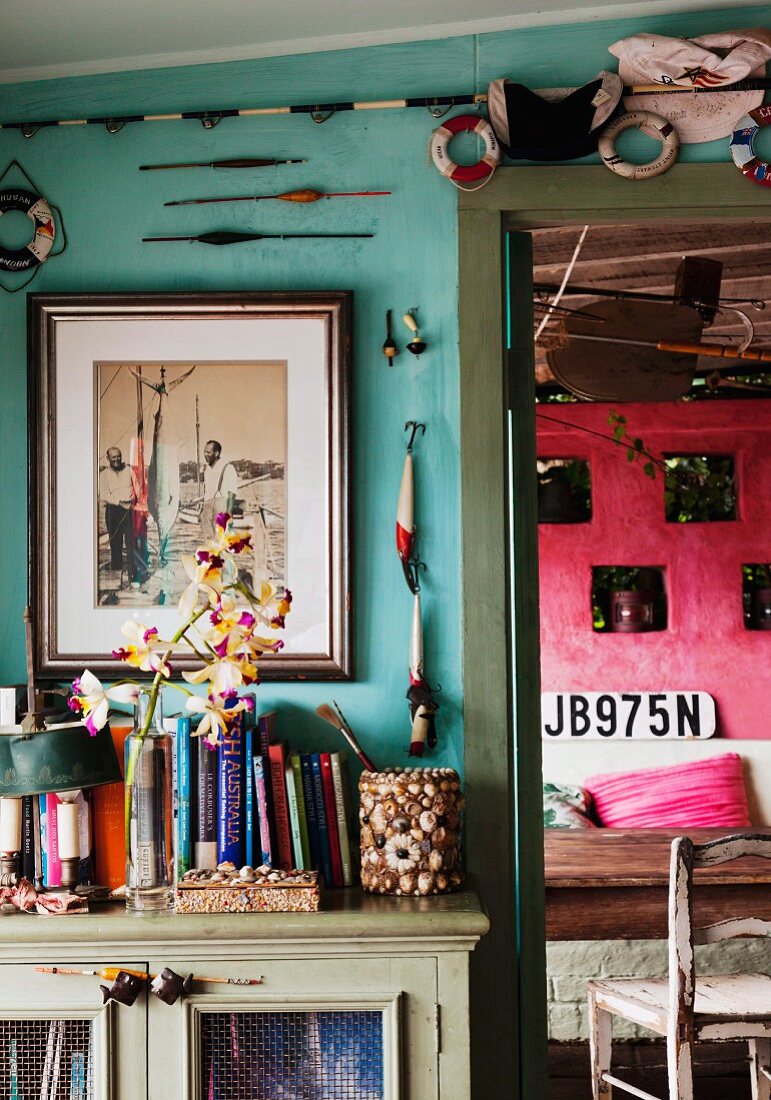 Books and maritime decorations on turquoise wall above vintage cabinet; view of pink wall to one side