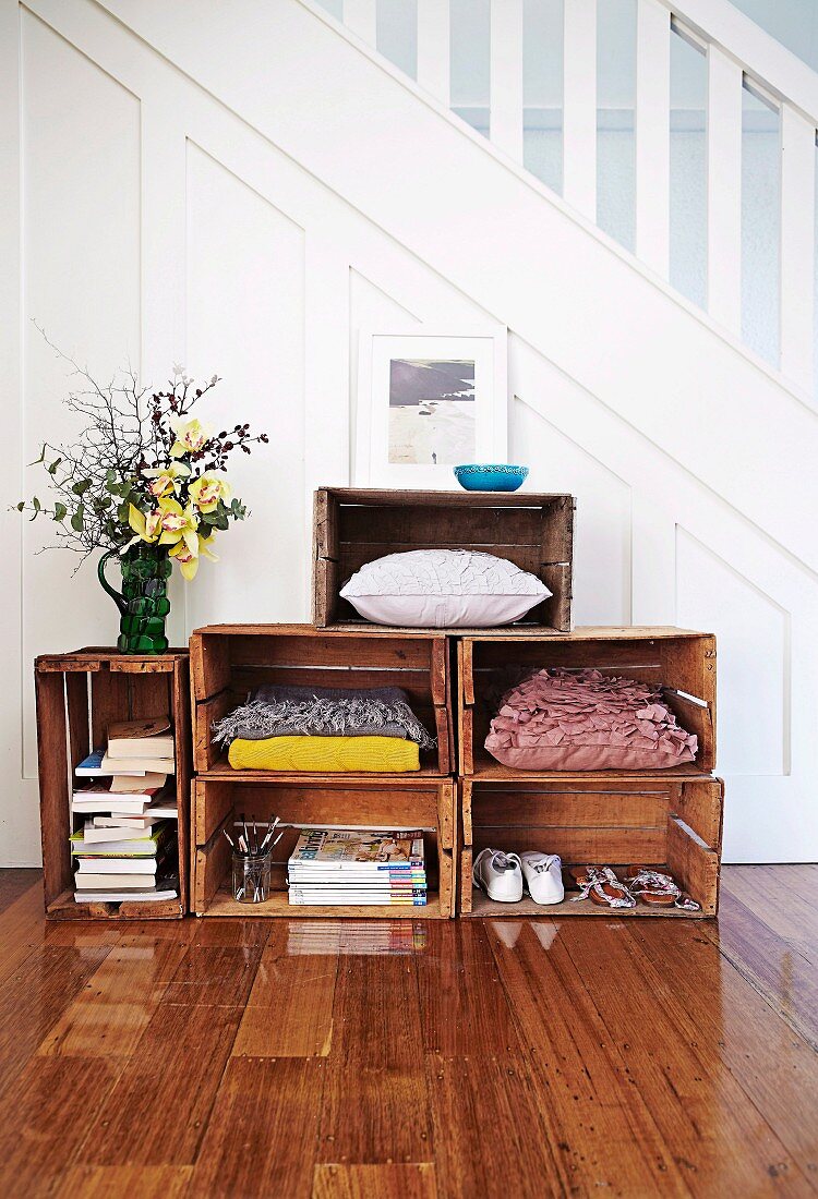 Vintage wooden crates used as shelving for books, shoes and cushions in spacious hallway of 20's house with white, classic wooden staircase