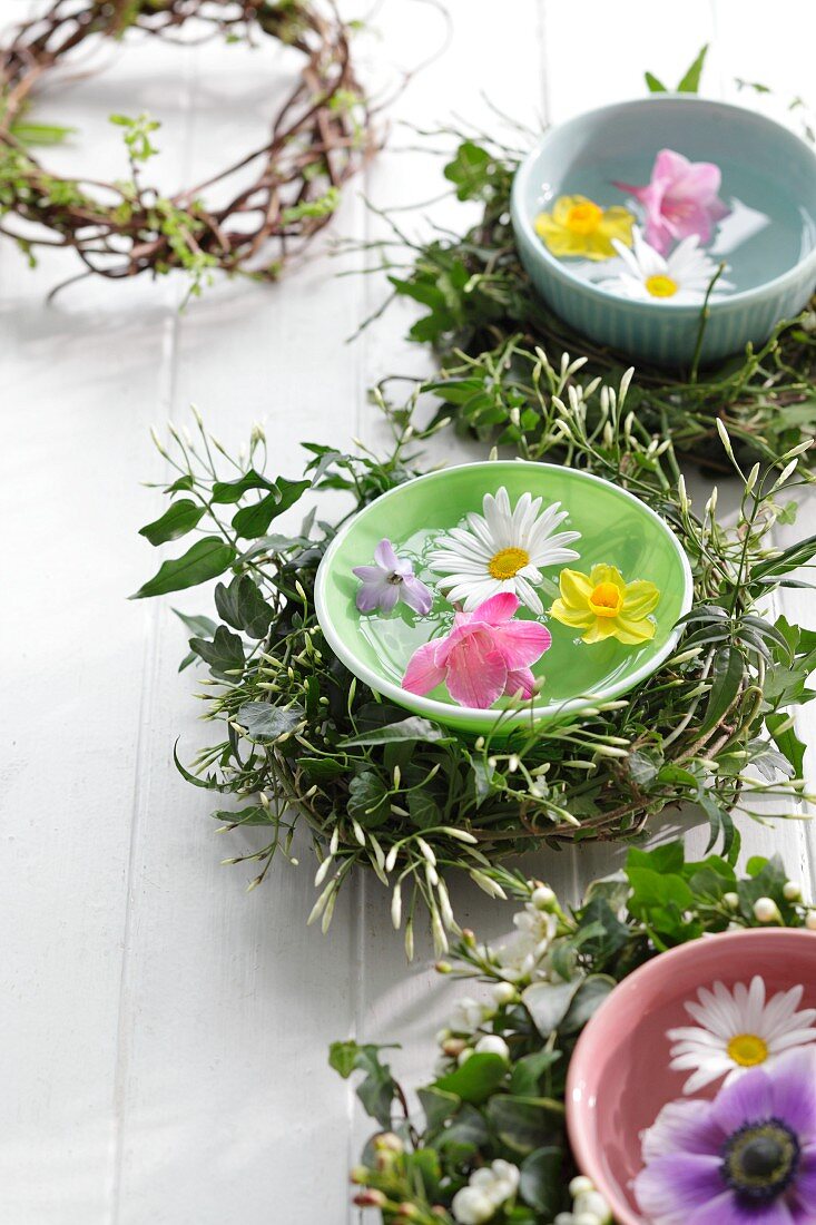 Bunte Wasserschalen mit schwimmenden Frühlingsblüten und Kränzen