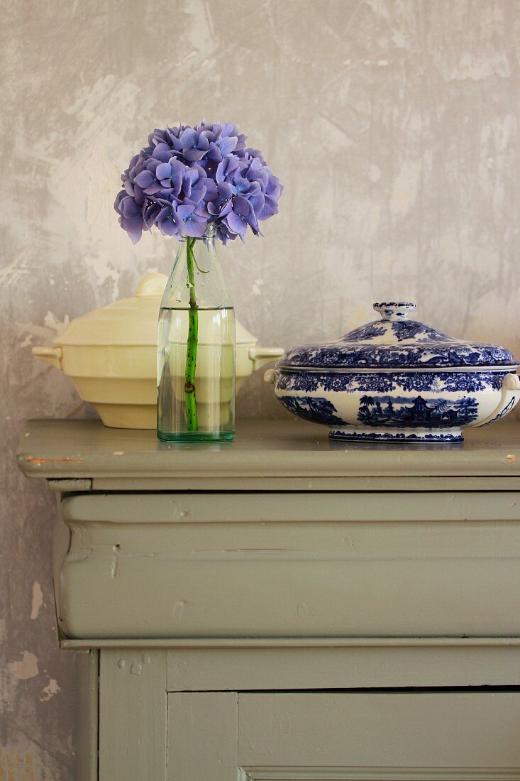 Flasche mit Hortensie und zwei Suppenschüsseln auf Vintage Unterschrank