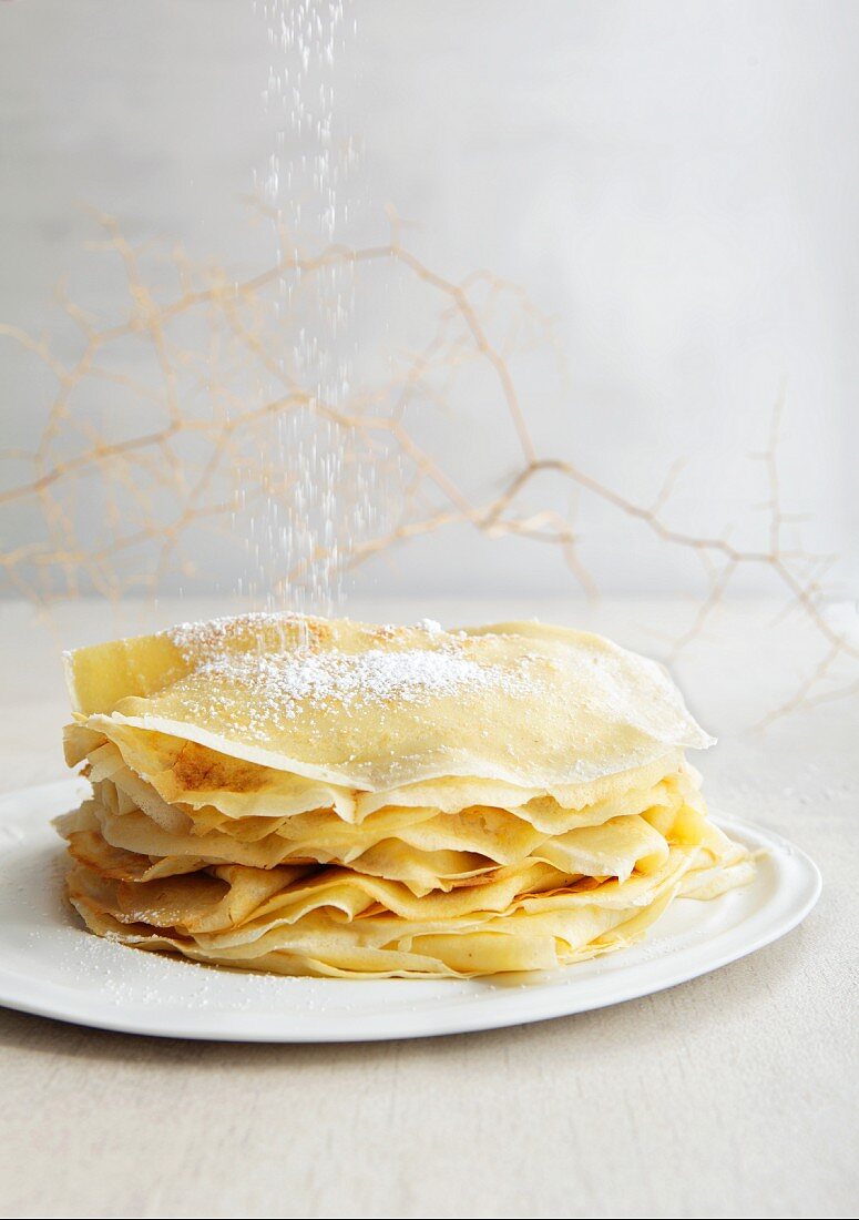Icing sugar being dusted onto a stack of crepes